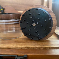 Wooden and black textured object on a wooden surface with a glass container in the background.