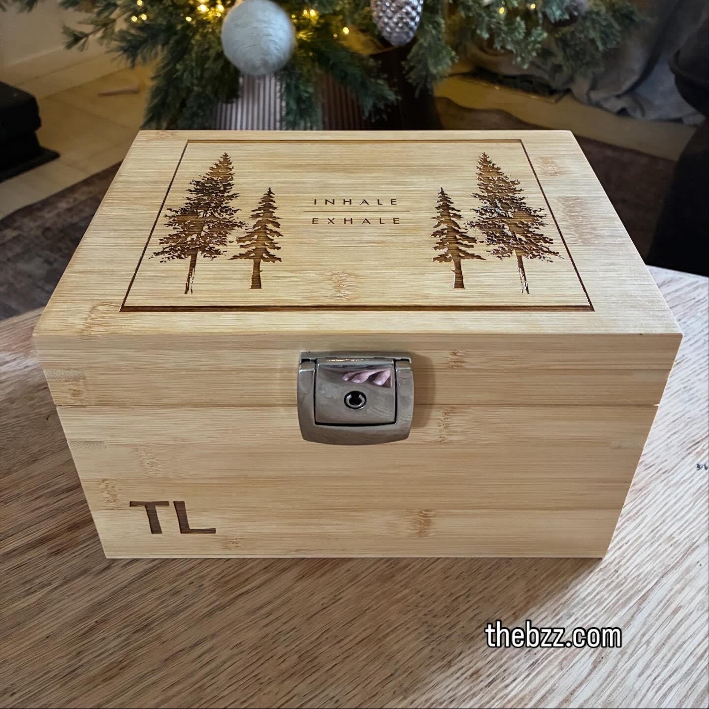 Wooden box with engraved trees and initials, placed in front of a decorated Christmas tree.