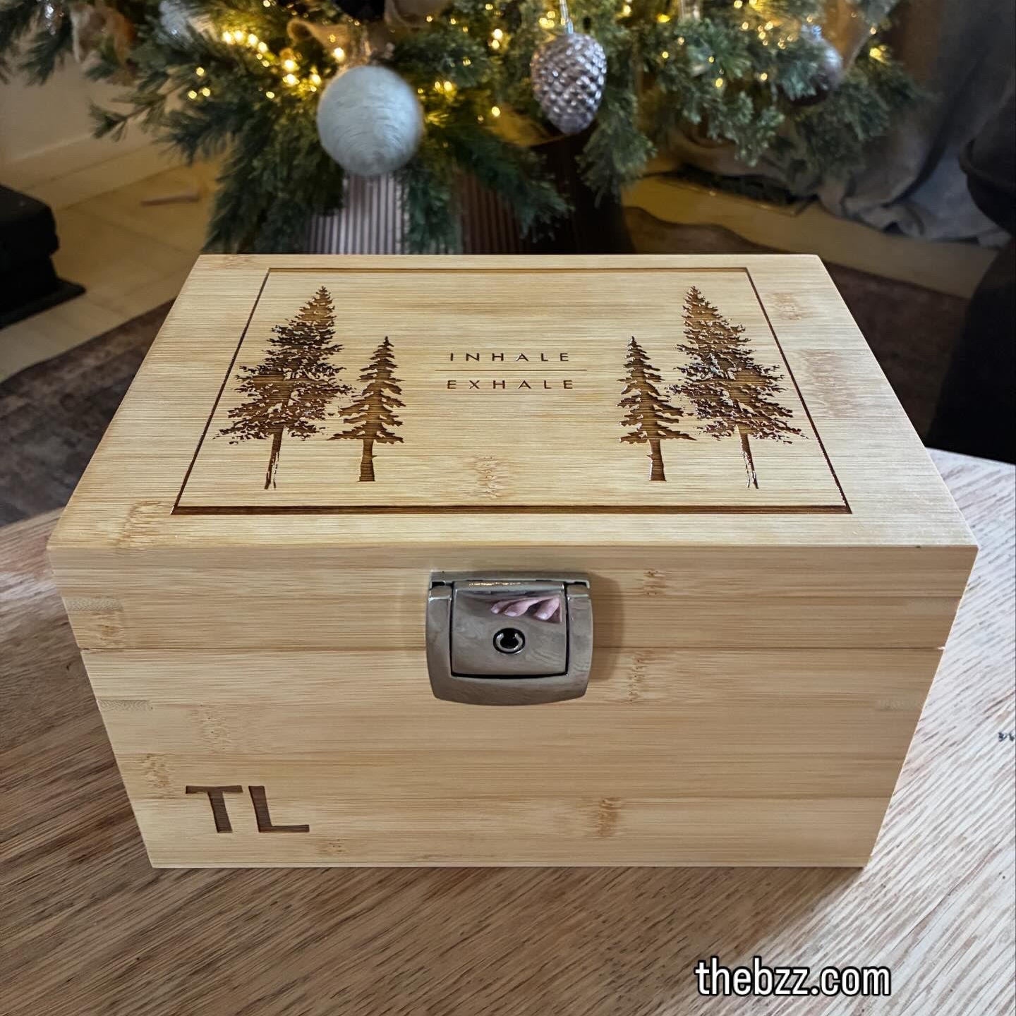 Wooden box with engraved trees and initials, placed in front of a decorated Christmas tree.