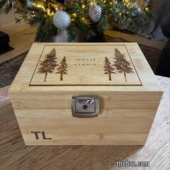 Wooden box with engraved trees and initials, placed in front of a decorated Christmas tree.